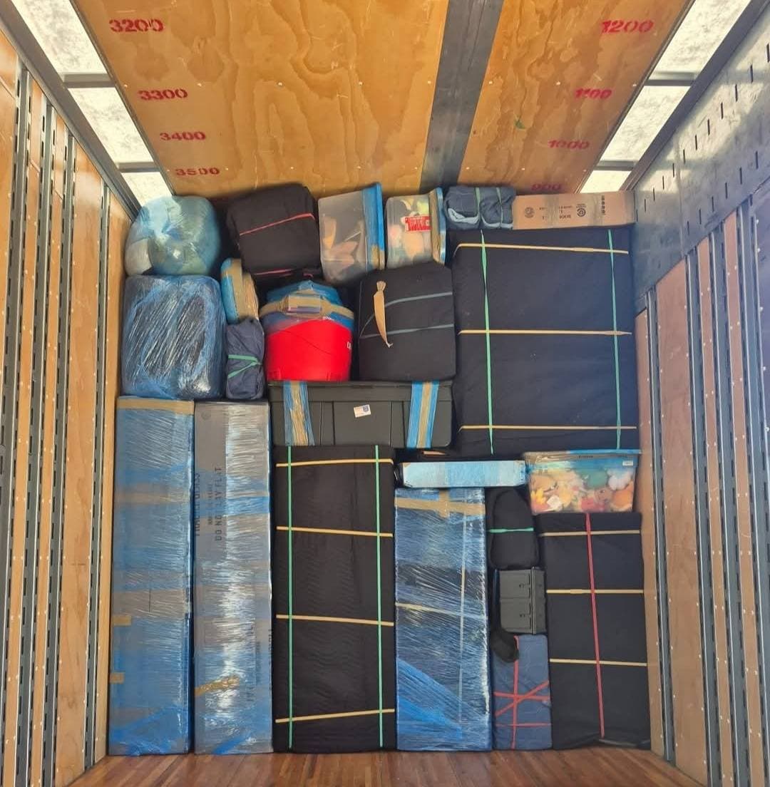 Moving truck interior packed with boxes and furniture wrapped in blue plastic and black blankets.